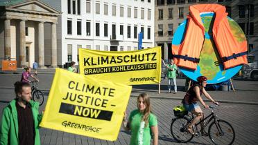 Aktivisten in Berlin vorm Brandenburger Tor, sie zeigen einen Globus mit angelegter Rettungsweste