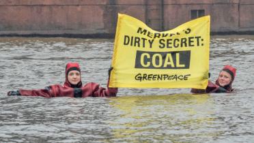 Im Hansaport in Hamburg halten Schwimmer ein Banner mit der Aufschrift "Merkel's Dirty Secret: Coal".