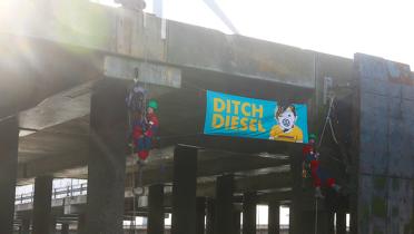 "Ditch Diesel"-Banner im Hafenbecken von Sheerness mit Kletterern