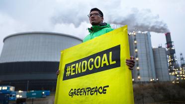 Greenpeace-Aktivist mit Handbanner "End Coal" vor Kohlekraftwerk