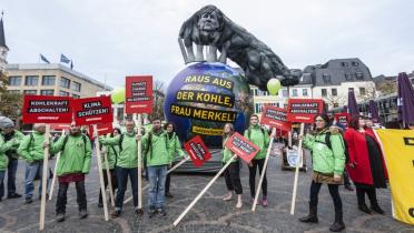 Aktivisten mit Bannern vor Merkel-Skulptur