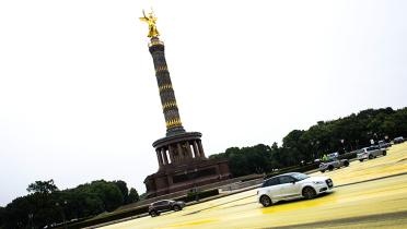 Autos im Kreisverkehr, Siegessäule im Hintergrund, gelber Asphalt