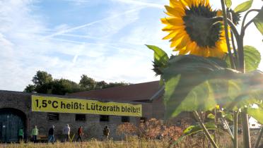 Sonnenblume vor Hof mit Banner: "1,5 Grad heißt: Lützerath bleibt"