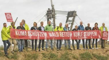Mitglieder der Kohlekommission protestieren mit roten Banner vor dem Braunkohletagebau in Hambach