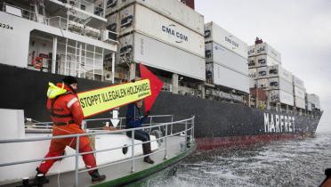 Greenpeace-Aktivisten auf einem Schlauchboot zeigen mit einem Pfeil auf ein Containerschiff