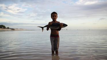Ein kleiner Junge steht im Wasser und hält einen großen Fisch auf dem Arm. 