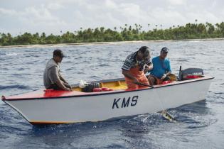 In einem kleinen Fischerboot ziehen Männer einen Fisch an der Leine aus dem Wasser