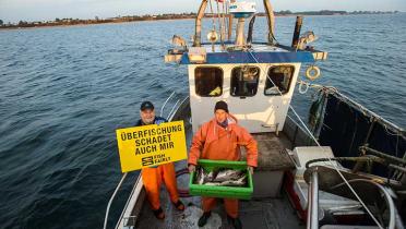 Kleinfischer Wolfgang Albrecht hält au seinem Kutter ein Protestschild "Überfischung schadet auch mir"