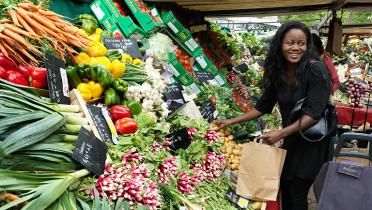 Junge Frau steht lachend an einem Gemüsestand