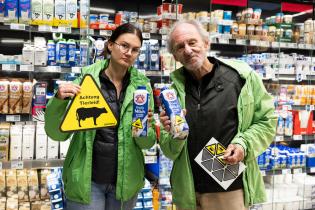 Zwei Greenpeace-Aktivist:innen im Supermarkt. Sie halten eine beklebte Bärenmarke-Milchpackung in die Kamera