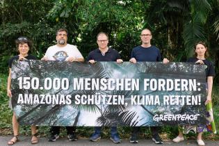 Greenpeace-Team und Carsten Schneider halten ein Banner mit der Aufschrift: 150.000 Menschen fordern: Amazonas schützen, Klima retten!