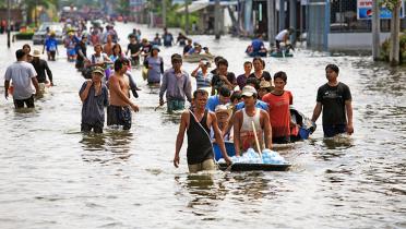 Menschen laufen auf einer überfluteten Straße nahe Bangkok, Thailand.