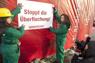 Greenpeace-Aktivisten bringen Banner "Stoppt die Überfischung" am riesigen Trawler Modell an, Dezember 2010
