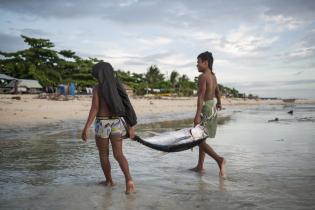 Zwei Kinder tragen einen gefangenen Fisch an den Strand. Das stellt ihre Lebensgrundlag dar. 