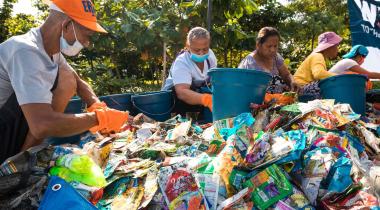 Menschen sitzen in Abfallbergen und sortieren den Plastikmüll