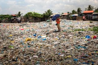 Frau steht inmitten von Müll am Strand bei Manila