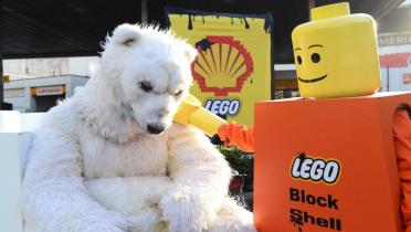 Ein Eisbär sitzt vor einer Tankstelle, neben ihm ein überdimensioniertes Legomännchen.