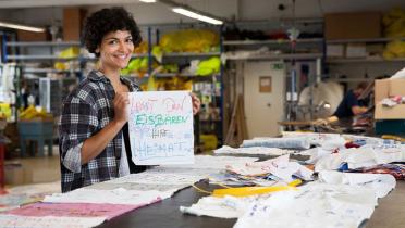Greenpeace-Mitarbeiterin hält Stofffetzen mit der Aufschrift "Lasst den Eisbären ihre Heimat" in die Kamera, vor ihr ein Holztisch mit schon sortierten Lappen.