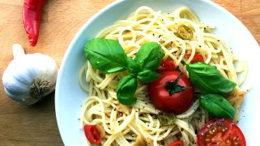 Teller mit Spaghetti in Knoblauchöl mit frischem Basilikum, Tomaten und Chili.