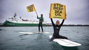 Zwei Greenpeace-Aktivisten auf Surfbretter im Wasser mit Plakaten gegen Tiefseebohrungen