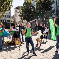 Aktive in grünen Greenpeace-Shirts sammeln auf einem Platz Müll