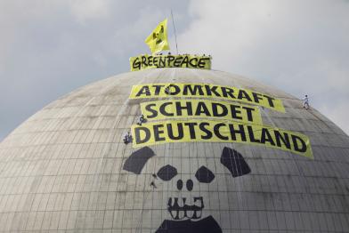 Greenpeace Aktivist:innen malen einen Totenkopf, der vom Symbol für die Radioaktivität umschlossen ist. Auf dem Banner steht: “Kernkraft schädigt Deutschland”