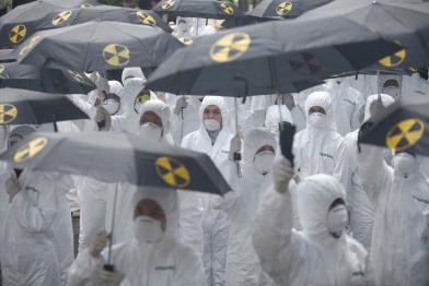 Aktion zum Fukushima-Jahrestag: Greenpeace Aktivist:innen, die Strahlenschutzanzüge und Masken tragen, ziehen durch einige der belebtesten Orte Jakartas, um auf die Gefahren der Kernenergie hinzuweisen. Sie halten auch schwarze Regenschirme mit Nuklearsymbolen in der Hand. 