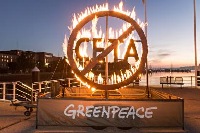 Greenpeace-Aktivist:innen demonstrieren mit einem brennenden CETA-Schild vor dem Kieler Landtag für mehr Widerstand gegen das europäisch-kanadische Handelsabkommen (CETA).