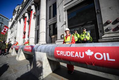 Klimaschützer:innen haben eine riesige Ölpipeline um das Gebäude gebaut. Sie trägt den Namen "Crudeau Öl". Kletterer:innen haben an zwei Eingangssäulen Banner mit der Aufschrift "Crudeau Öl Hauptquartier" heruntergelassen. 