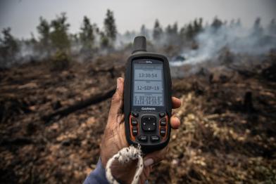 Hand mit GPS-Gerät mit Koordinaten eines Moorbrandes