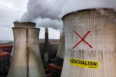 Luftaufnahme eines Greenpeace-Protests auf einem Kühlturm des RWE-Kraftwerks Neurath in Deutschland. Die Aktivist:innen haben ein 22 Meter großes "X" auf den 100 Meter hohen Kühlturm gemalt und darunter ein Transparent mit der Aufschrift "Shutdown" angebracht. 