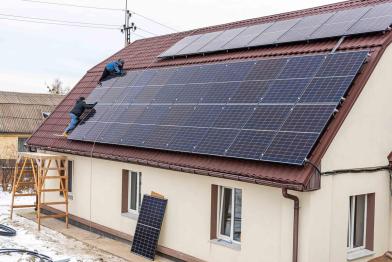 Zwei Arbeiter montieren die Solaranlage auf dem Dach eine wiederaufgebauten Krankenhauses in Horenka, Ukraine.