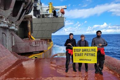 Drei Aktive protestieren auf Shell-Ölplattform, auf dem Banner: Stop Drilling, start paying