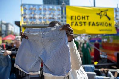Ein Mann hält auf einer Kleidertauschparty eine Hose hoch, im Hintergrund ein Banner: "Fight Fast Fashion"
