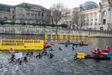 Aktive in Booten und im Wasser der Spree, große Buchstaben auf Schwimmbojen bilden den Schriftzug „Klimageld jetzt!“
