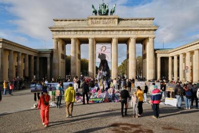  Passant:innen betrachten Kleiderstatue aus Textilmüll vor dem Brandenburger Tor