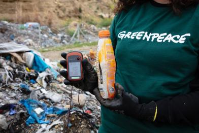 Greenpeace-Aktivistin hält ein GPS-Gerät und eine Plastikflasche auf einer Mülldeponie in der Türkei.