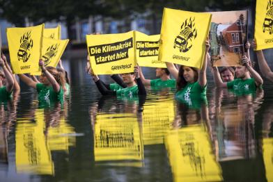 Vor Messeeingang IAA 2021: 15 Greenpeace-Aktive stehen in einem 100 mal 90 Meter großen Wasserbecken und halten Fotos von Extremwetter und Banner „Die Klimakrise startet hier“ 