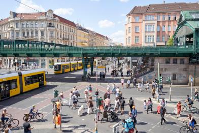 Verkehrssituation an einer Kreuzung in Berlin: zwei Straßenbahnen, eine Bahnbrücke, Radfahrende und Fußgänger:innen 
