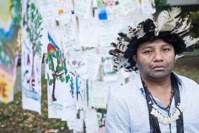 Indigenensprecher Adriano Karipuna vor der brasilianischen Botschaft. Im Hintergrund kleine Flaggen, die Menschen aus ganz Deutschland in den vergangenen Monaten gestaltet und an die brasilianische Regierung adressiert haben.