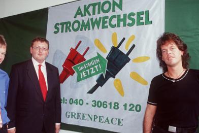 Drei Personen vor einem Plakat mit der Aufschrift "Aktion Stromwechsel"