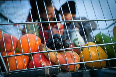Obst und Gemüse im Einkaufswagen - im Hintergrund ein Kind und eine erwachsene Person.