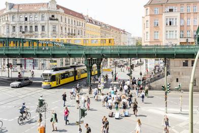 Verkehr in Berlin: S-Bahn, Straßenbahn, Fußgänger und Fahrradfahrende auf einer Kreuzung.