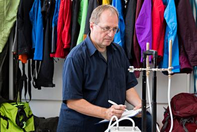 Greenpeace-Chemieexperte Manfred Santen bei Datennahme Raumluftmessung, dahinter Outdoorkleidung