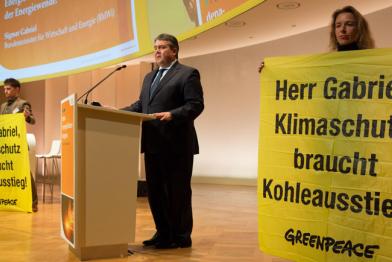 Gabriel bei einer Rede, auf beiden Seiten stehen Greenpeace-Aktivisten mit Plakaten