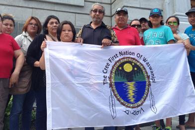 Eine Gruppe von Cree-Indianern hält ein Banner, auf dem das Logo der Waswanipi-Gemeinde zu sehen ist.  