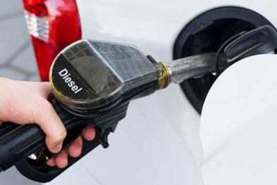 Eine Hand hält einen Zapfhahn mit der Aufschrift Diesel. Der Hahn steckt im Tank eines Autos.