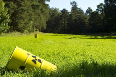 Eine Attrappe eines Atommüllfasses liegt auf einer Waldlichtung. Es wird auf die vergebliche Suche nach einem Endlager hingewiesen. 