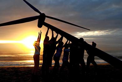 Ein Windrad wird vor einem Sonnenuntergang am Strand aufgestellt.