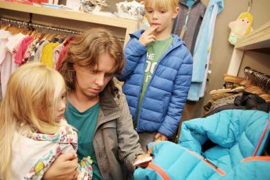 Eine Mutter mit ihren beiden Kindern beim Kauf von Kinderkleidung